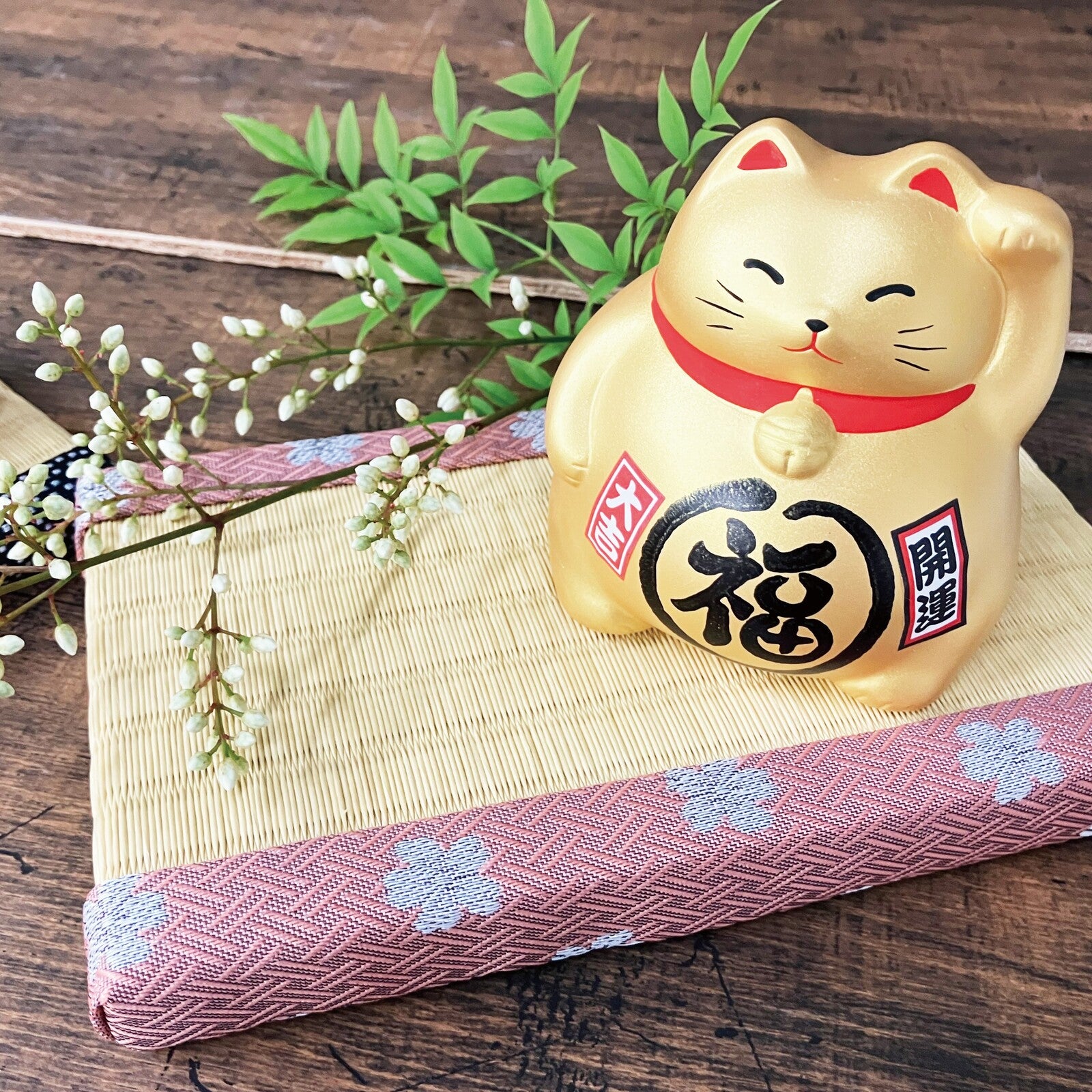 Gold cat-shaped ornament with red ribbon on a wooden surface with plants