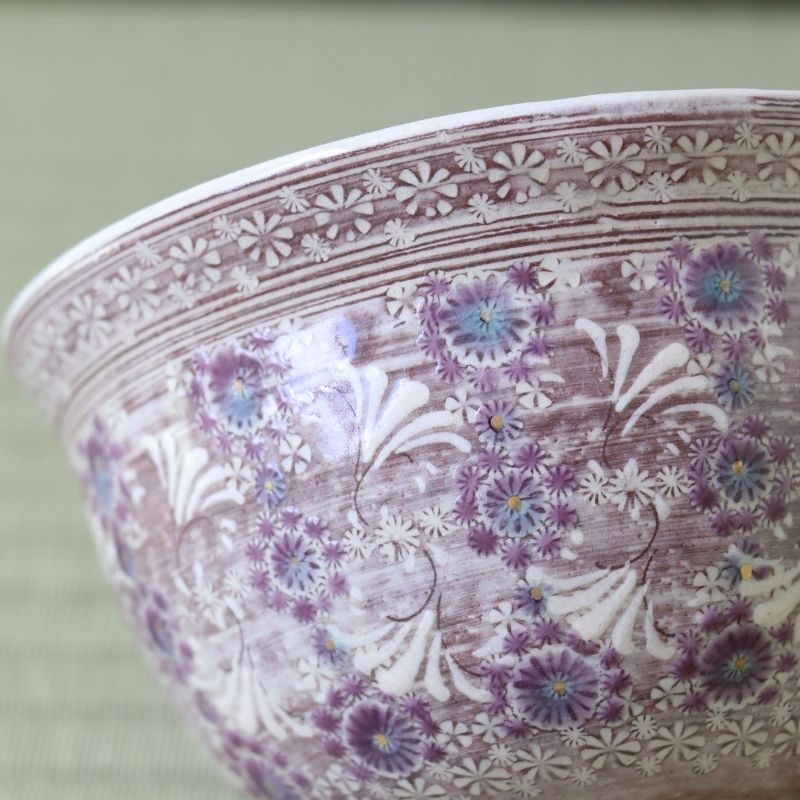 A close-up of a ceramic bowl featuring a textured, rustic brown and white floral pattern with purple and blue flower accents.