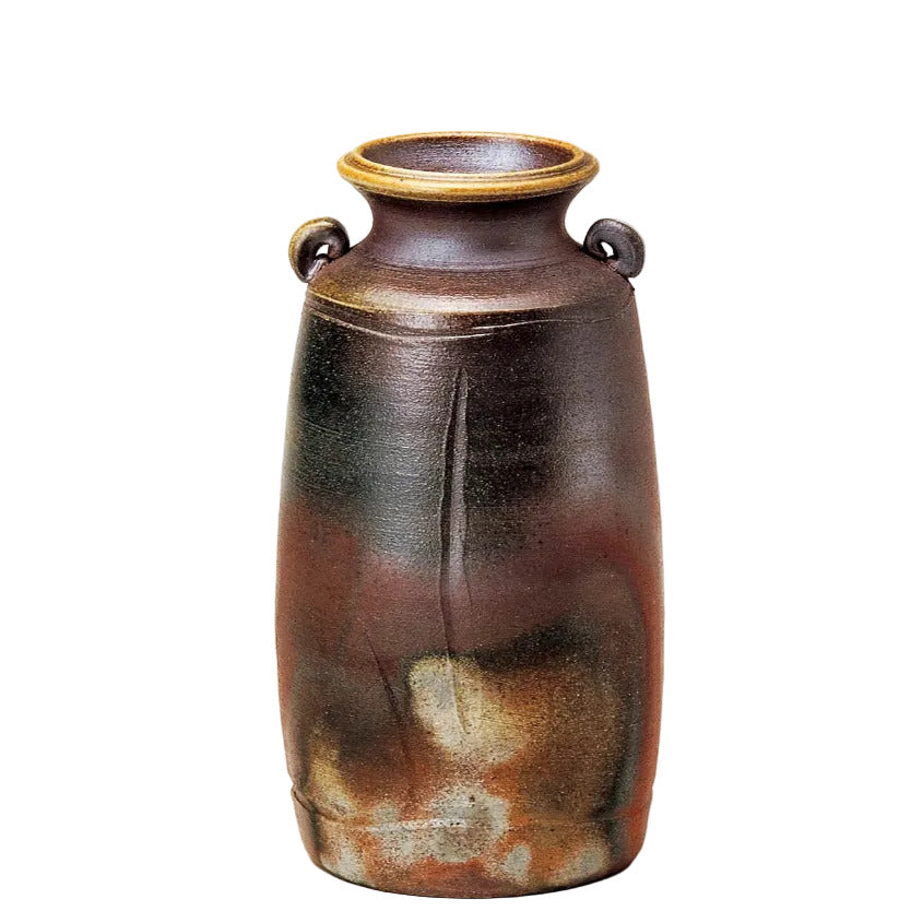 A rustic ceramic vase with a dark brown and black glaze, featuring a warm orange-brown mottled pattern near the base and a light beige rim, set against a plain light gray background.