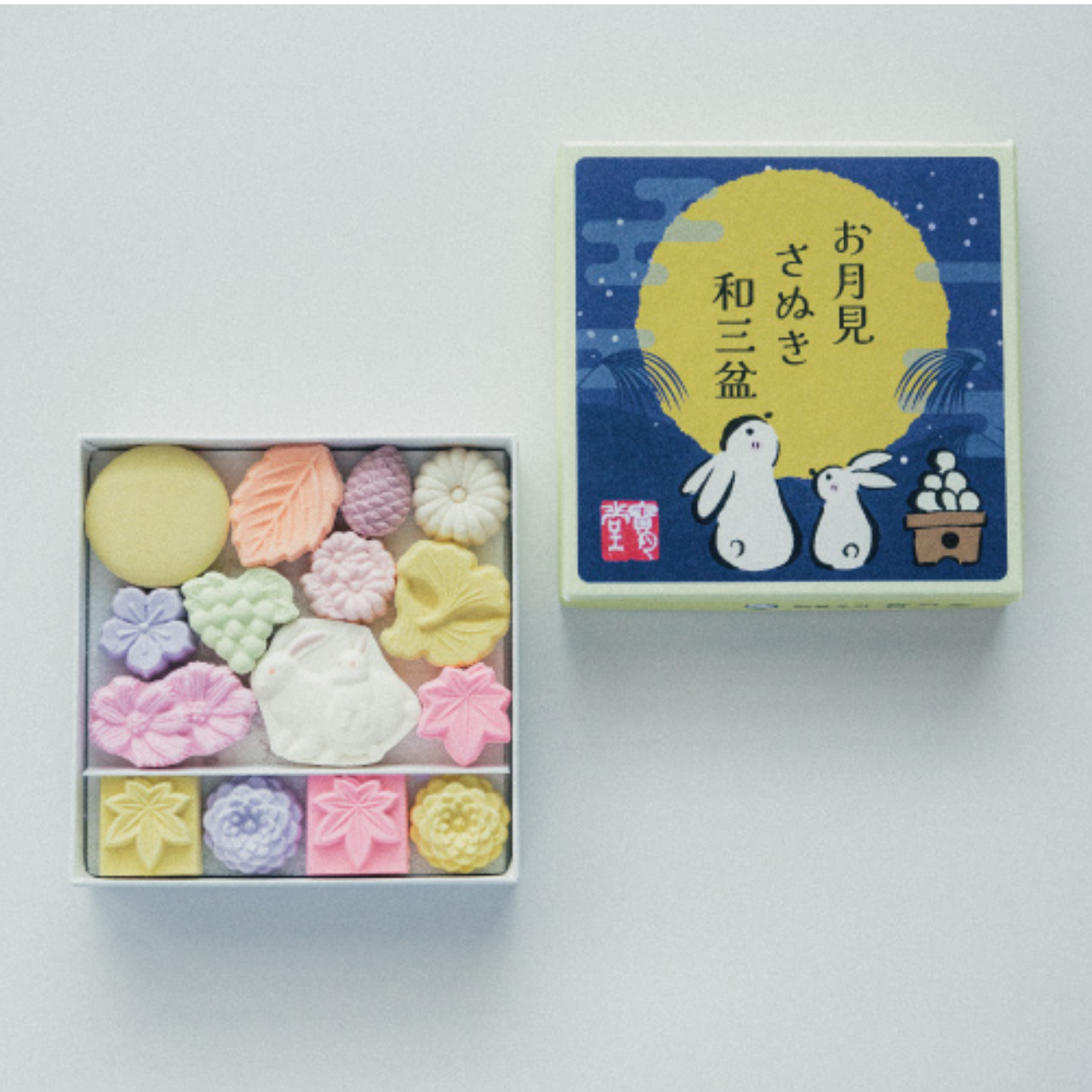 Box of colorful candy with a decorative box featuring cartoon characters and Japanese text on a light gray background.