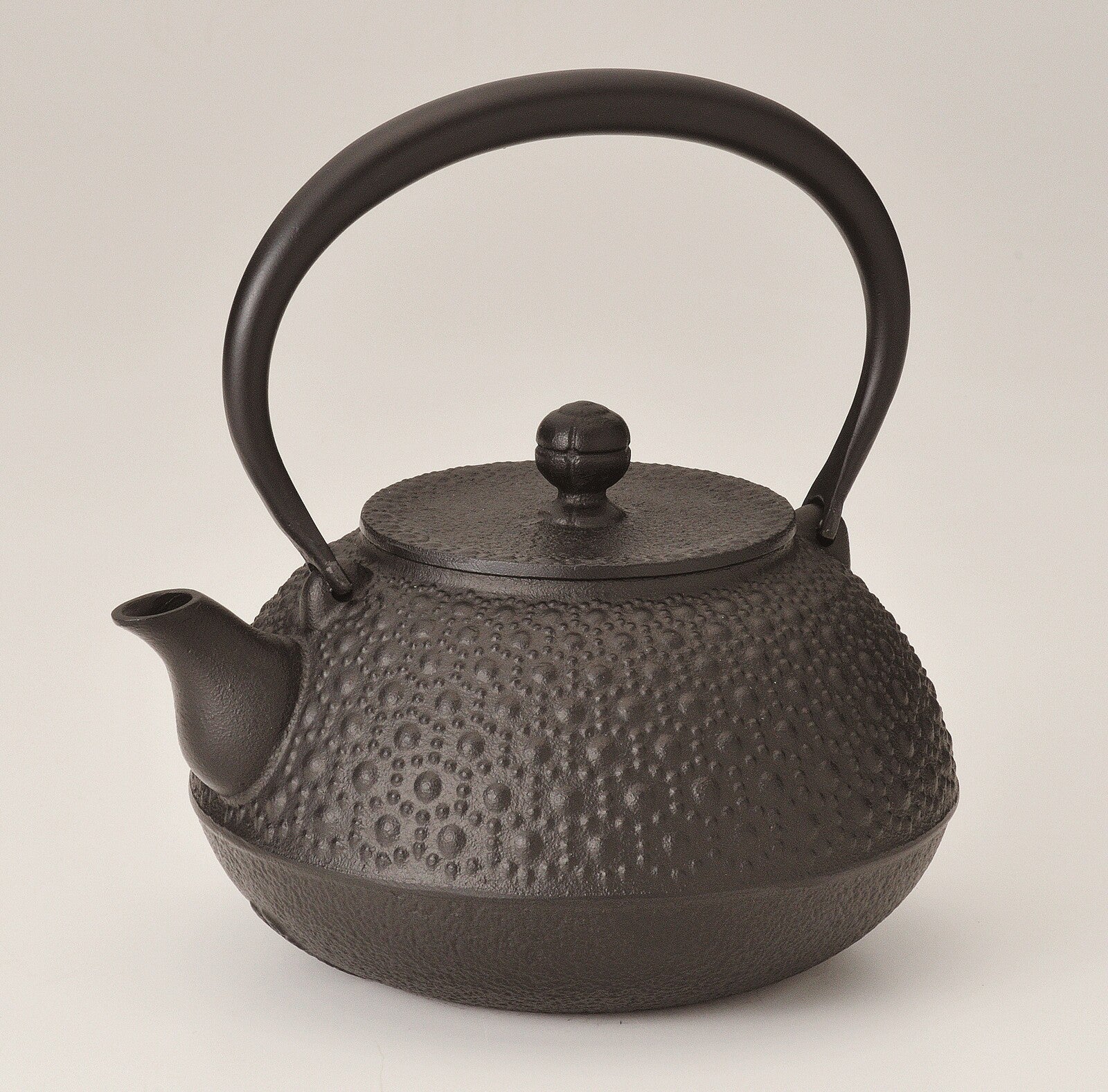 Black cast iron teapot with textured surface on a light beige background