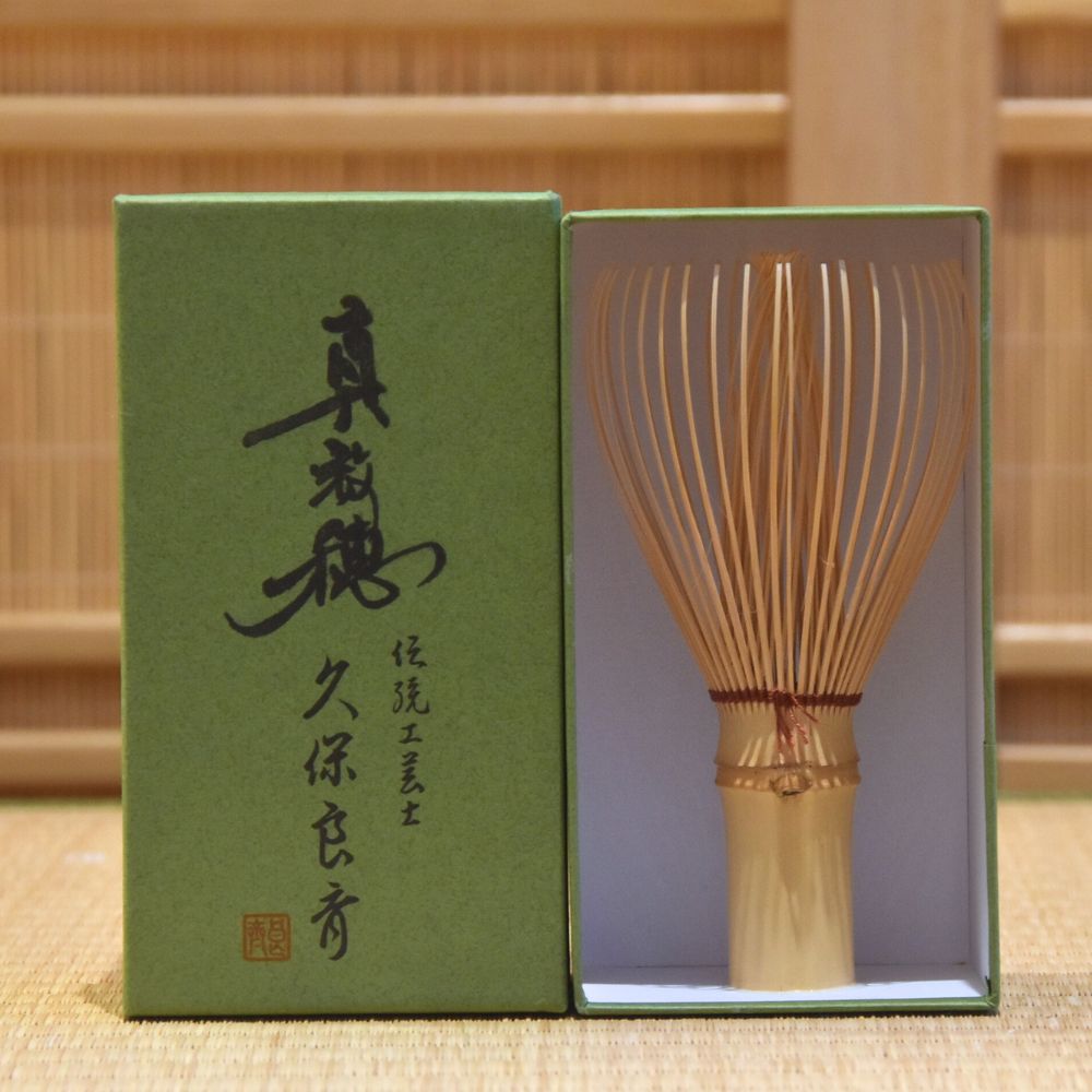 Bamboo whisk with green box featuring Japanese text on a wooden background