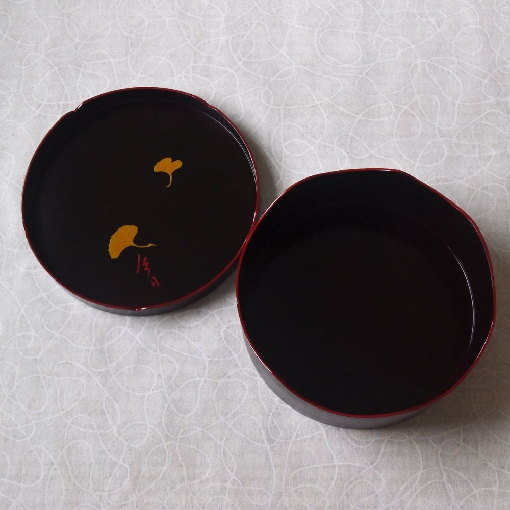 Two black ceramic plates with gold leaf design on a textured white background