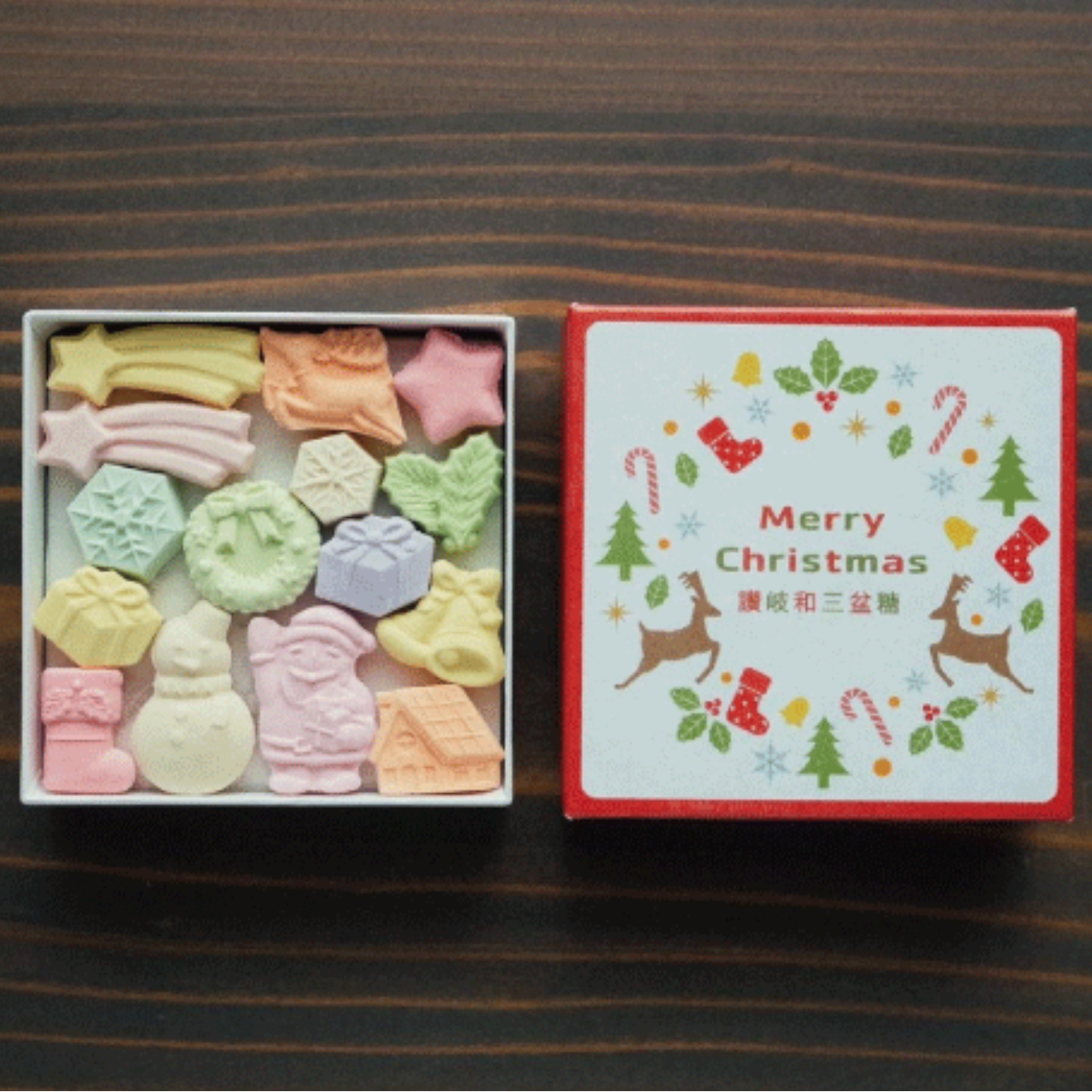 Box of colorful candy with a Christmas-themed card on a wooden surface