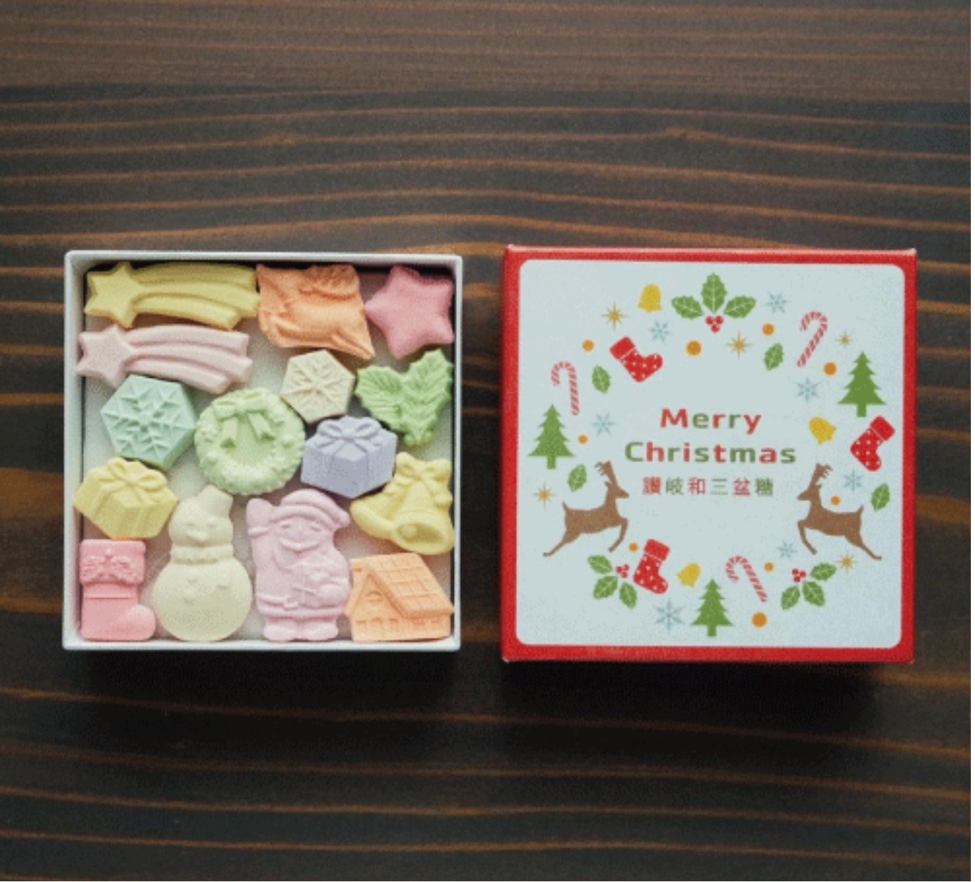 Box of colorful candy with a Christmas-themed card on a wooden surface