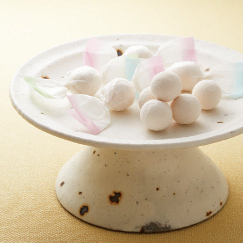 White ceramic cake stand with wasanbon higashi candy on a beige background