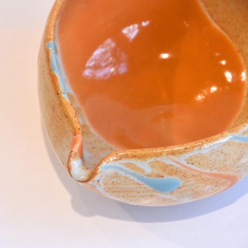 Ceramic bowl with orange interior and decorative exterior on a light background