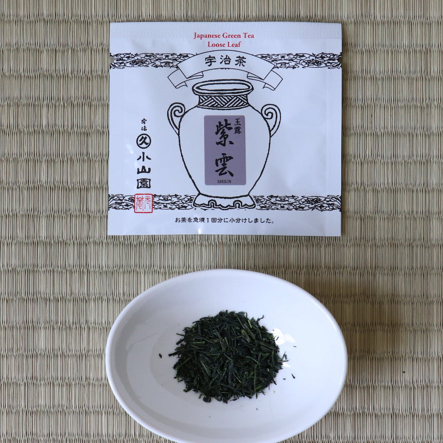 Tea leaves in a white bowl with a tea bag packaging on a woven mat