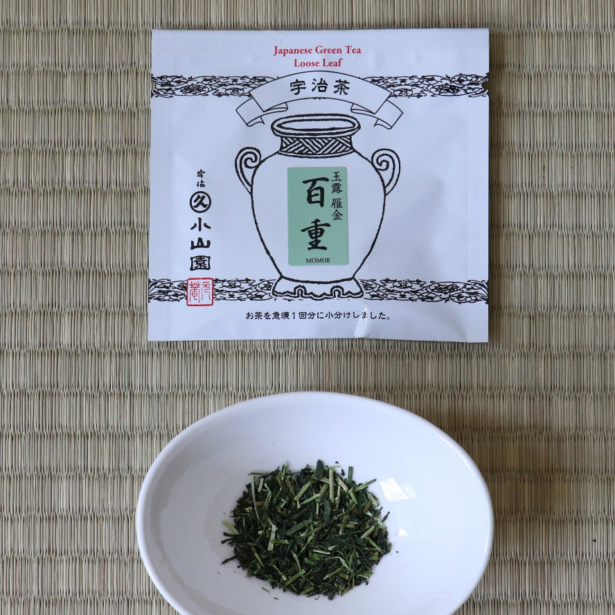 White bowl with green tea leaves and a tea package on a woven mat
