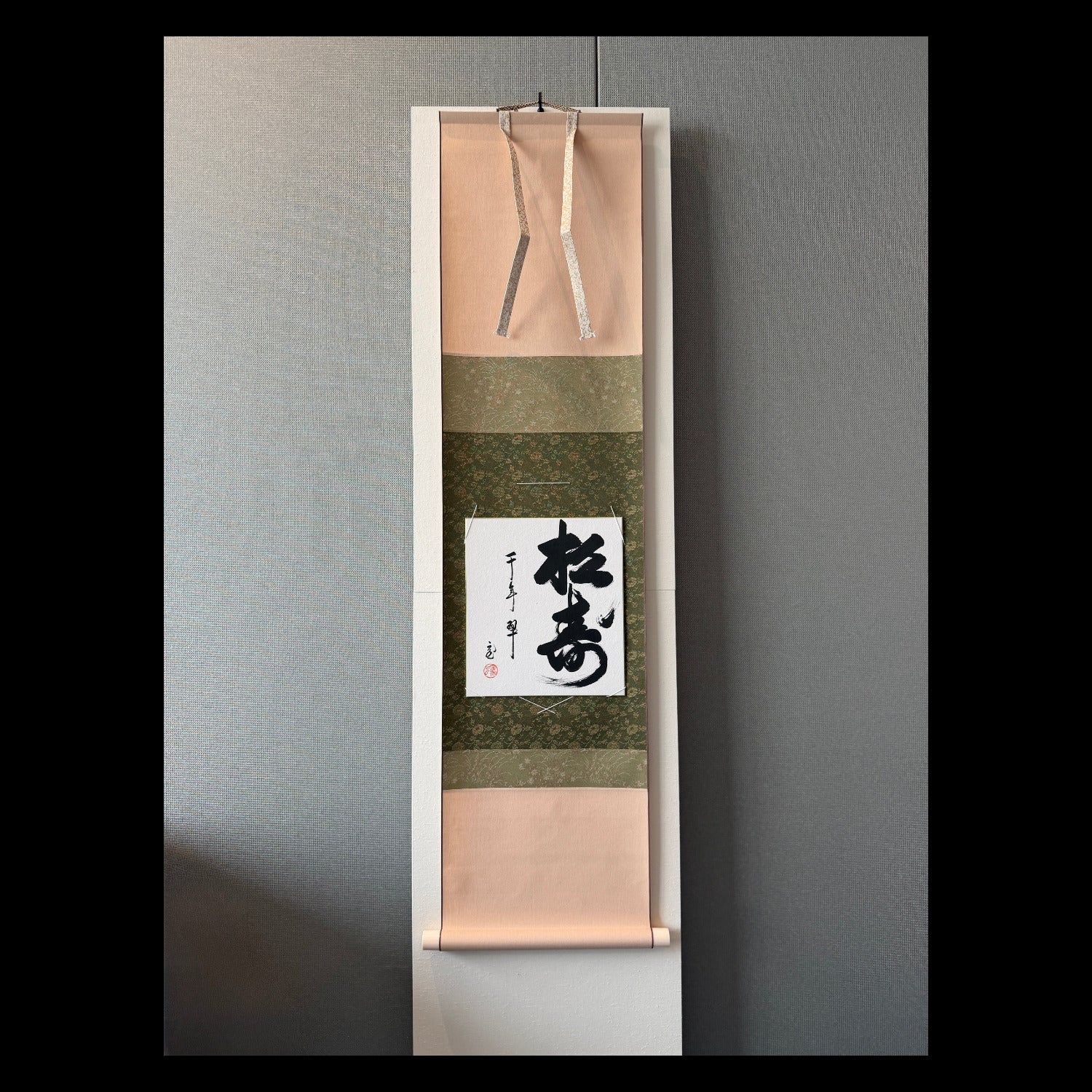 Vertical scroll with Japanese calligraphy on a gray wall