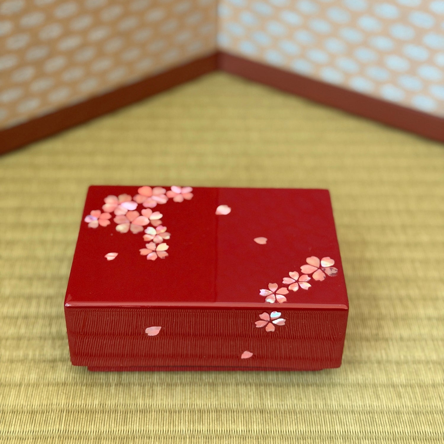 Red decorative box with cherry blossom patterns on a tatami mat floor.