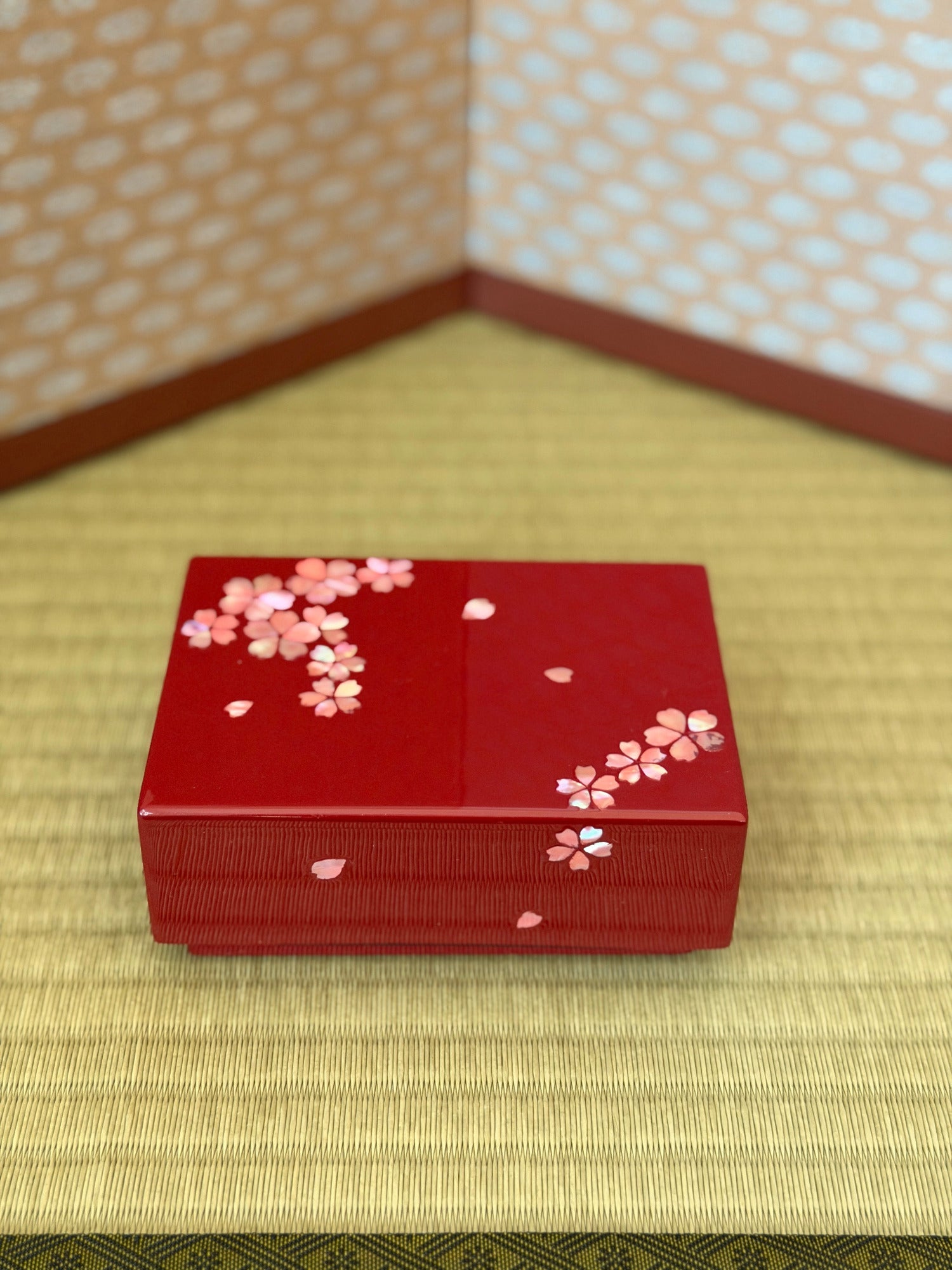 Red decorative box with cherry blossom patterns on a tatami mat floor.