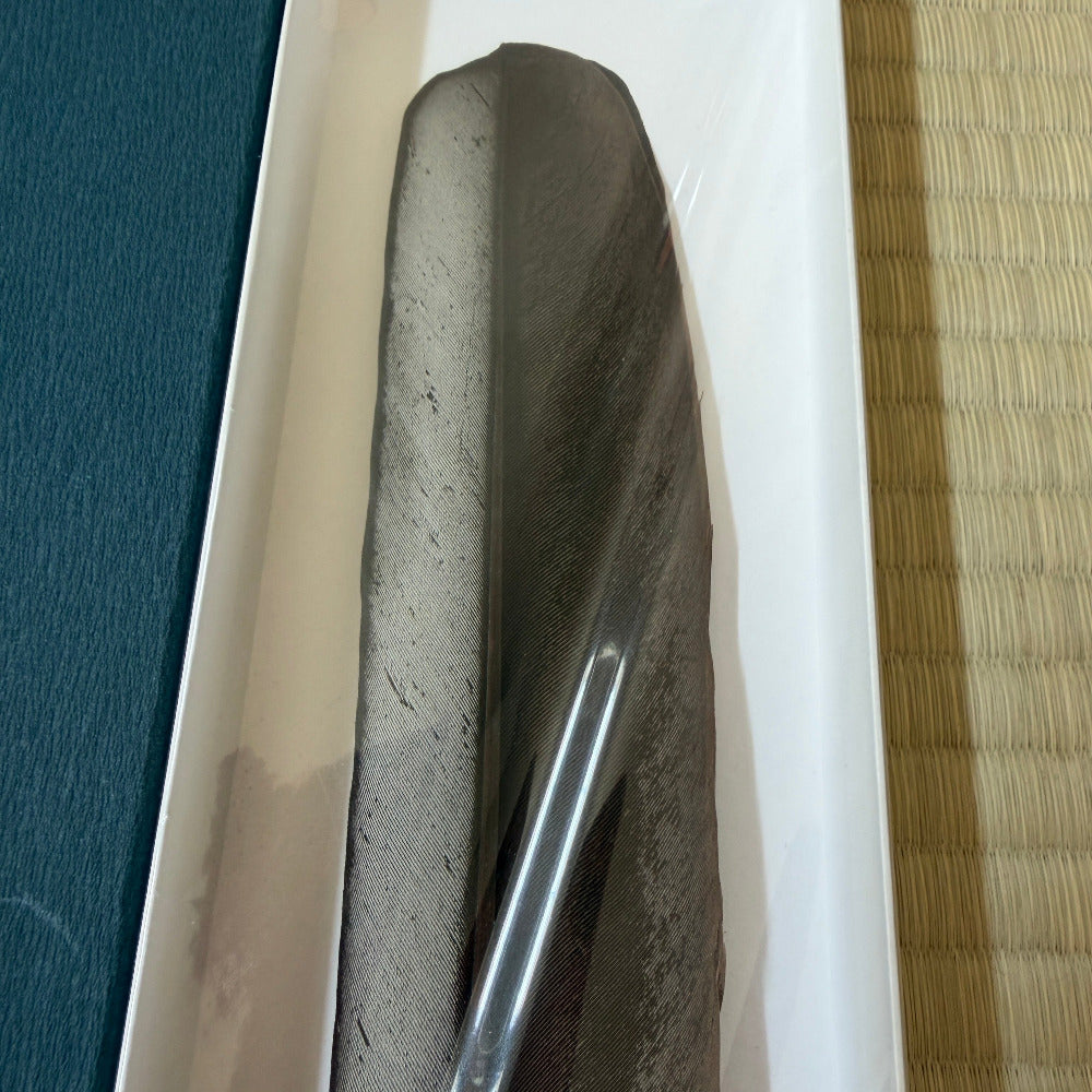 A dark gray textured stone or slate decorative piece inside a white rectangular tray, with a blue textured surface on the left and a tan woven mat on the right.