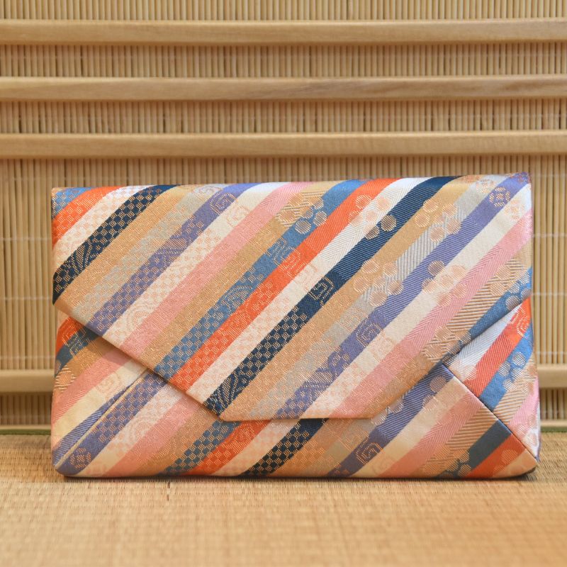 Colorful striped clutch bag by Kitamura Tokusai on a woven mat background