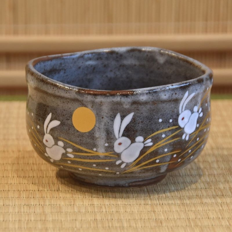 A traditional Japanese Kutani ware matcha bowl with a blue-gray glaze, featuring white rabbits and a golden moon motif on the exterior.