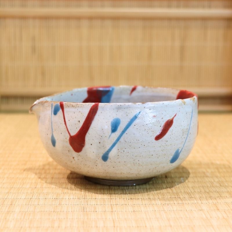 Ceramic bowl with red and blue abstract patterns on a woven mat