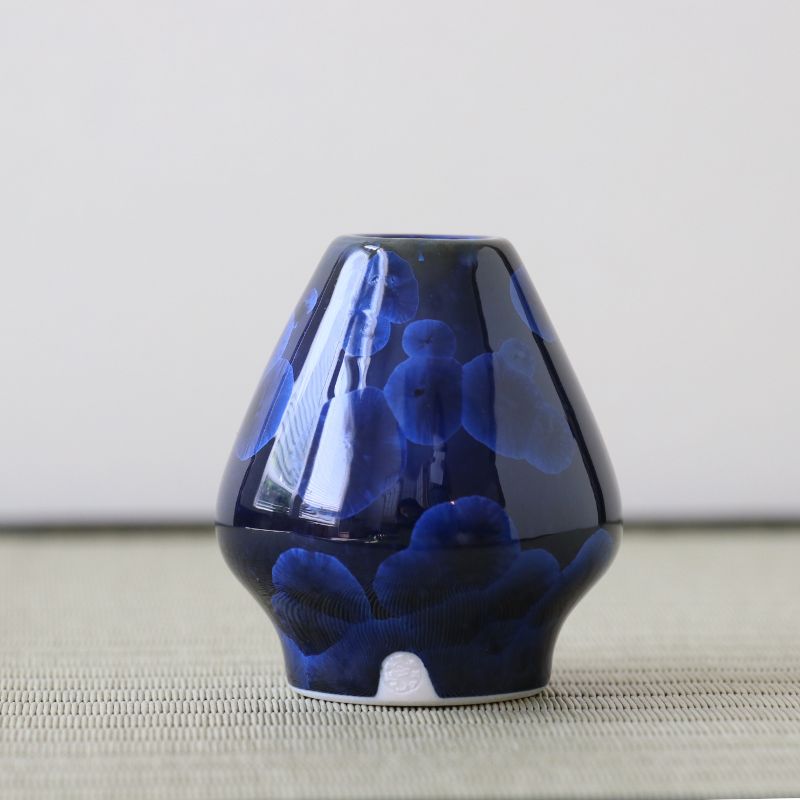 Blue Matcha whisk stand on a textured surface with a neutral background