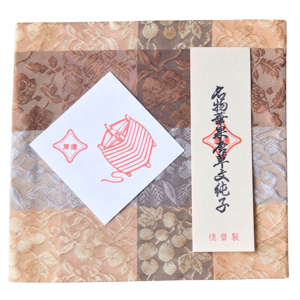 Decorative box with a white card featuring a red illustration of yarn and text on a patterned background.
