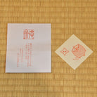 Two red stamps on white paper and beige card against a bamboo mat background