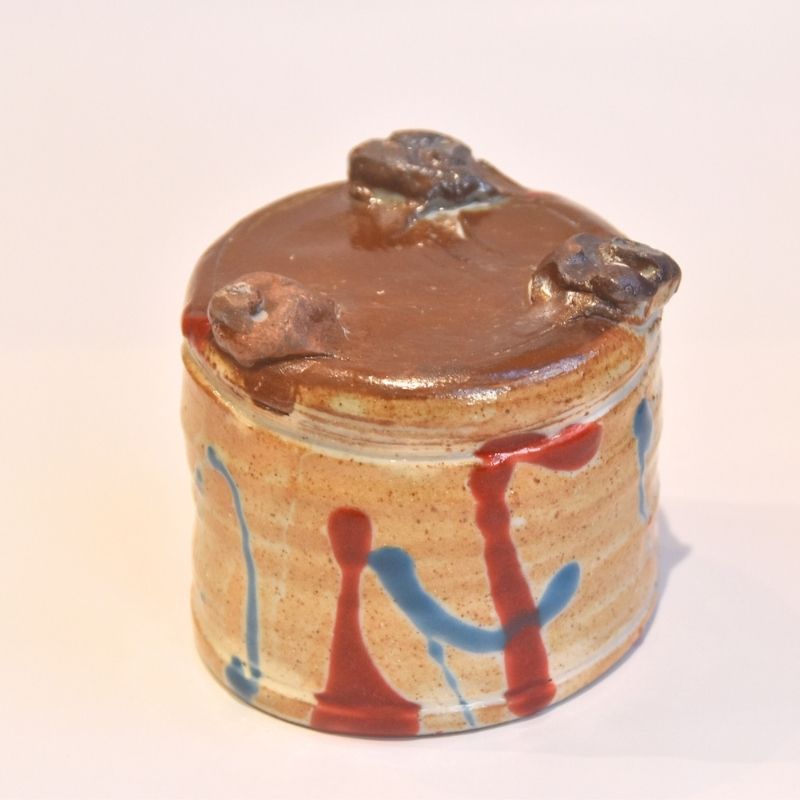Small ceramic jar with a lid featuring animal shapes on a white background