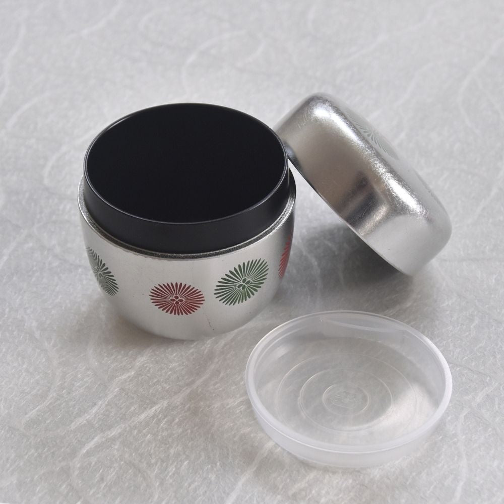 Tea container with black, silver, and clear lids on a textured white surface.