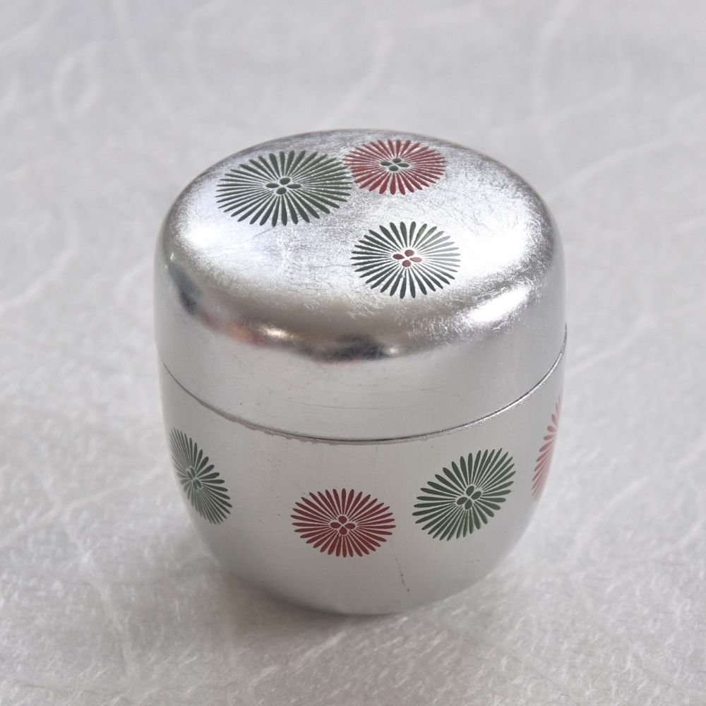 Silver container with floral patterns on a textured white background
