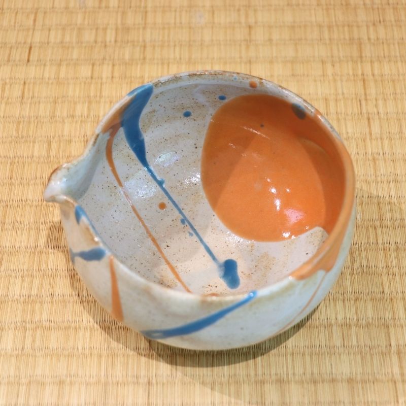 Ceramic bowl with orange and blue design on a woven mat
