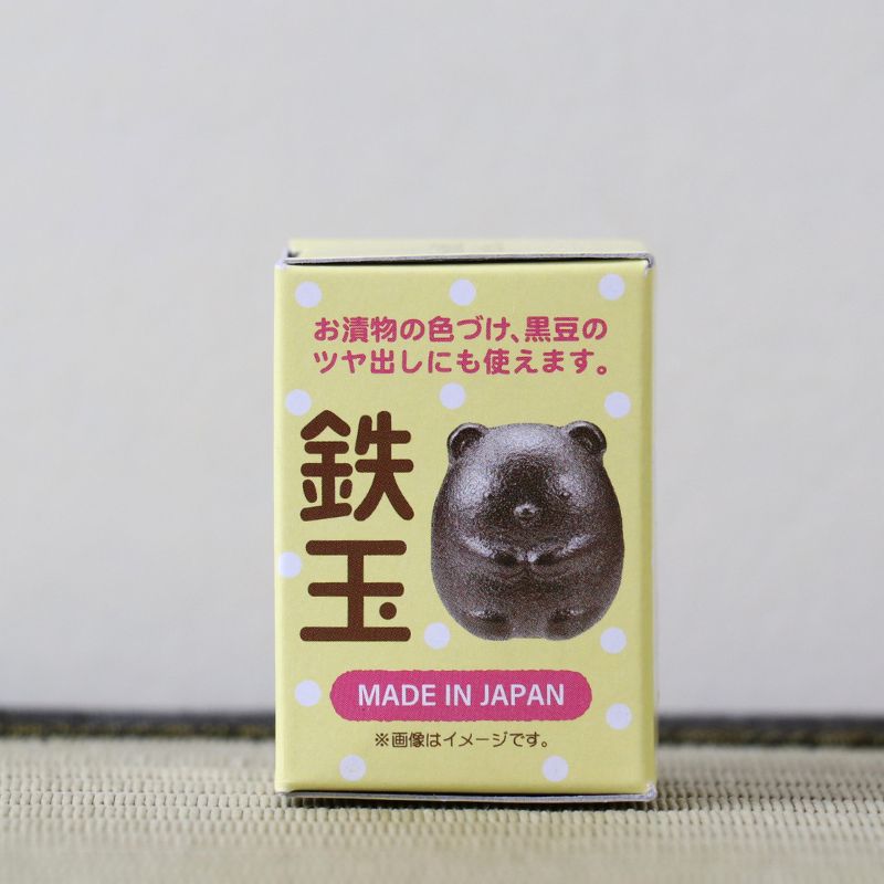 A small yellow product box with Japanese text, a dark brown bear-shaped item printed on the front, and a pink 'MADE IN JAPAN' label, standing on a textured beige surface against a light gray background.