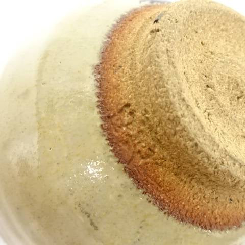 Close-up of the chawan foot showing the textured unglazed clay, reddish firing line, and pale ash glaze surrounding the base.