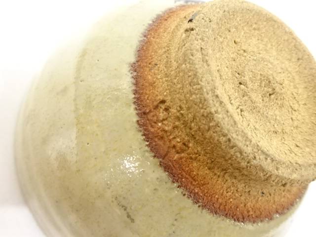 Close-up of the chawan foot showing the textured unglazed clay, reddish firing line, and pale ash glaze surrounding the base.