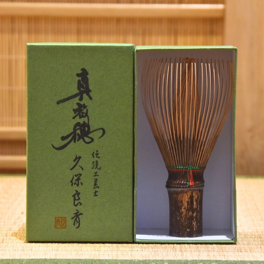 Black Bamboo whisk in a green box with Japanese text on a wooden background
