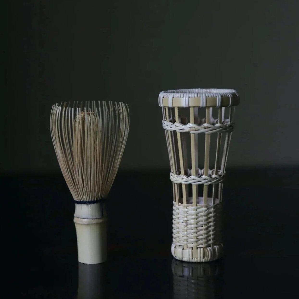 Two woven tea-making tools on a dark surface with a dark background