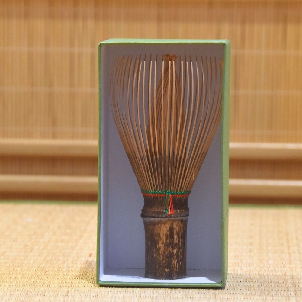 Black Bamboo whisk upright in a box with a beige bamboo mat background