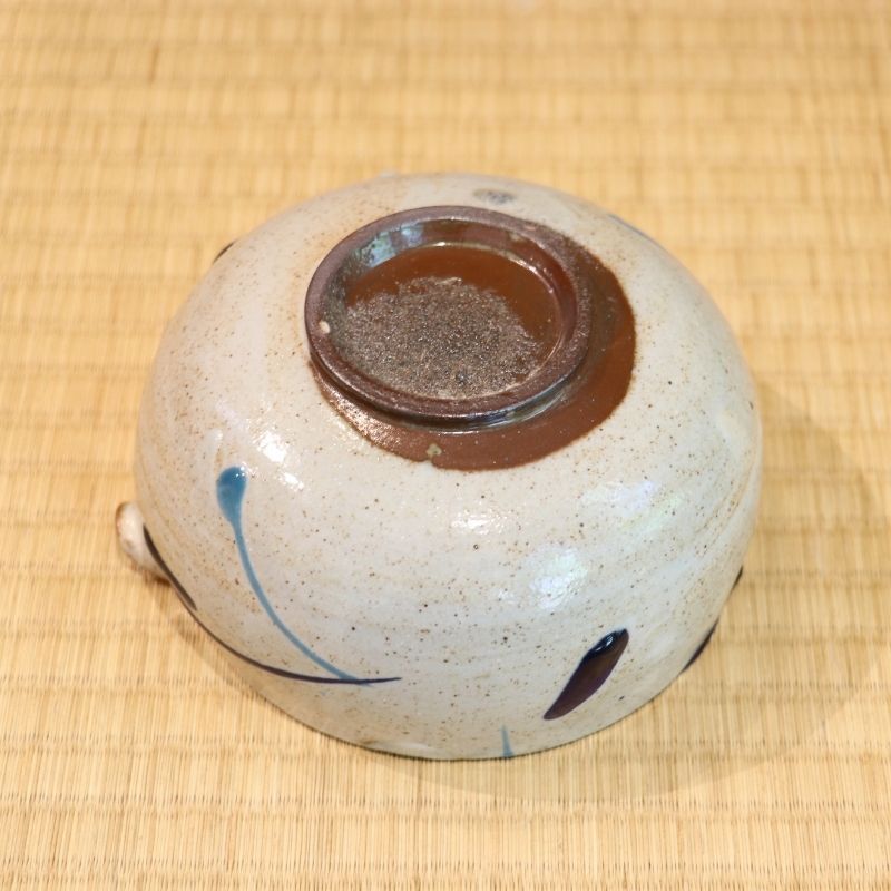 Underside view of the hand-painted Tamba Ware bowl showing its exposed brown clay foot and speckled ivory glaze with blue accents.