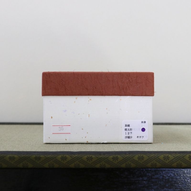 A small rectangular product box with a terracotta-colored textured top and a white body, photographed upright on a patterned surface against a plain light background.