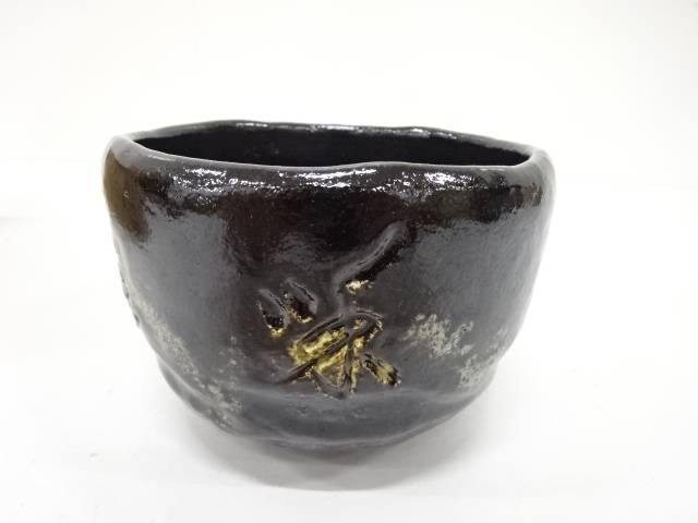 Front view of the Eiko Meido matcha bowl showing its softly irregular rim, smoky black glaze, pale markings, and gold botanical brushwork.