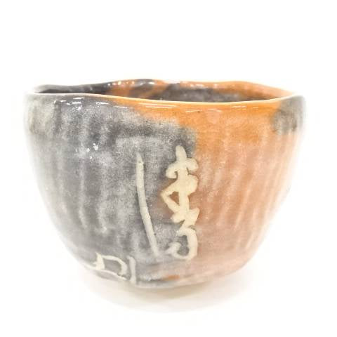 Front view of the Eiko Meido Raku chawan showing smoky gray glaze, warm orange firing tones, and flowing white calligraphic brushwork.