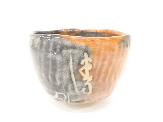 Front view of the Eiko Meido Raku chawan showing smoky gray glaze, warm orange firing tones, and flowing white calligraphic brushwork.