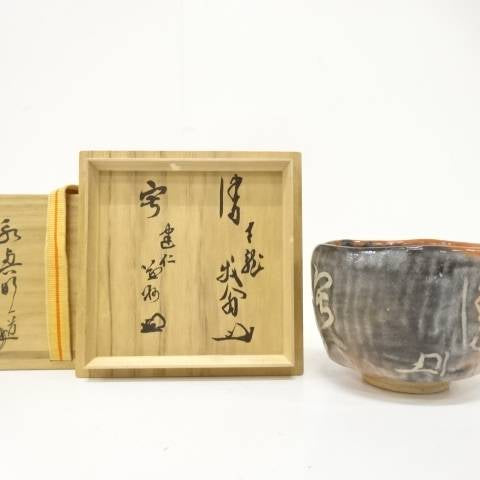Pre-owned Eiko Meido Raku matcha bowl with smoky charcoal and ember-orange glaze displayed beside its inscribed wooden storage box components.