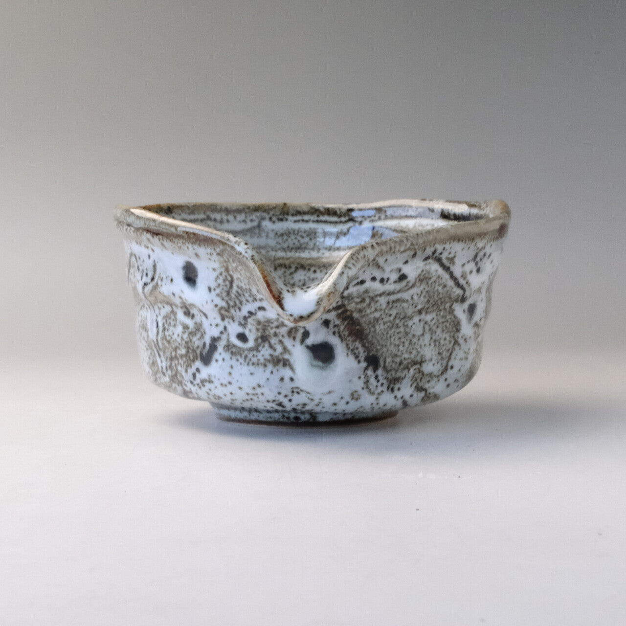 Front view of the Mino Ware katakuchi matcha bowl with its V-shaped pouring spout centered above the speckled white and gray surface.