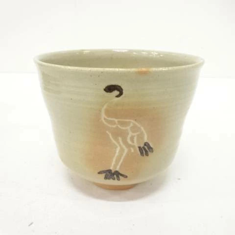 Front view of the Hiroshi Fukumori chawan showing a graceful standing crane against a warm ivory glaze with subtle ochre tones near the foot.