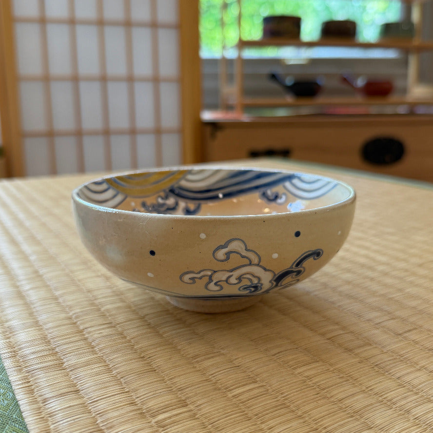 Side view of the hand-painted wave matcha bowl displayed on tatami, with the cobalt and ochre design wrapping around the rim and exterior.