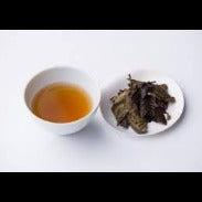 Tea cup with brewed tea and a plate of tea leaves on a white background