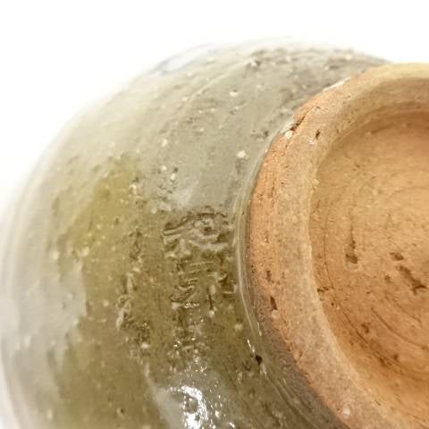 Close-up of the chawan foot showing the unglazed clay base, irregular firing texture, and translucent ash-green glaze along the edge.