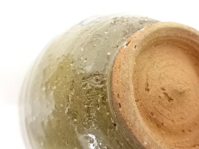 Close-up of the chawan foot showing the unglazed clay base, irregular firing texture, and translucent ash-green glaze along the edge.