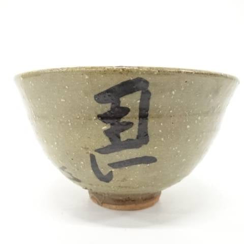 Front view of the Izumino Ware matcha bowl showing bold black Hidari-Uma calligraphy against an earthy ash-green speckled glaze.