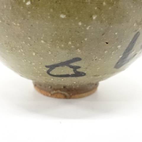 Close-up of the lower exterior showing a small dark painted mark, pale speckled glaze, and warm exposed clay around the foot.