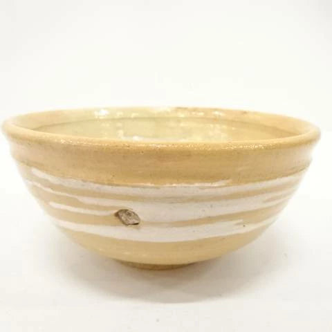 Front view of the Kahei Shima Raku chawan showing its softly irregular rim and layered sand, cream, and ivory glaze.