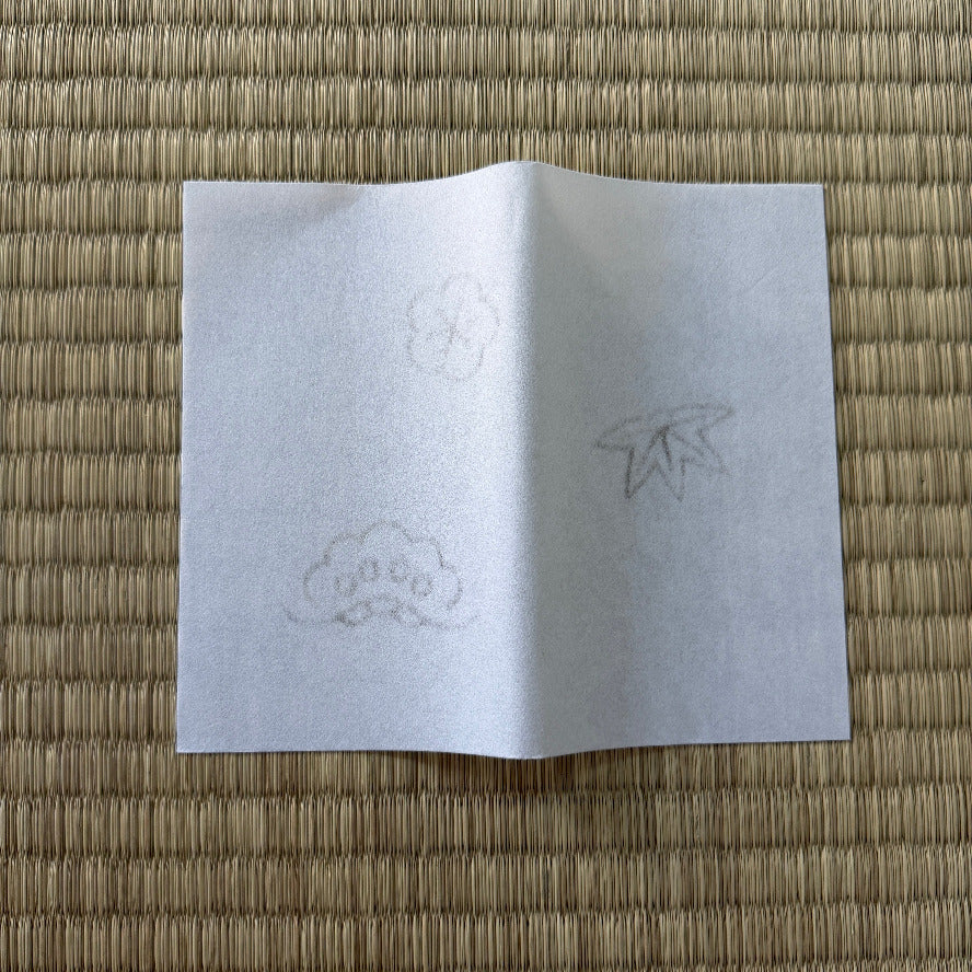 White paper with cloud and leaf drawings on a woven mat background