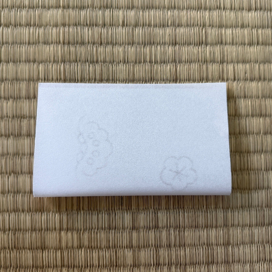 White rectangular object with embossed designs on a woven mat background